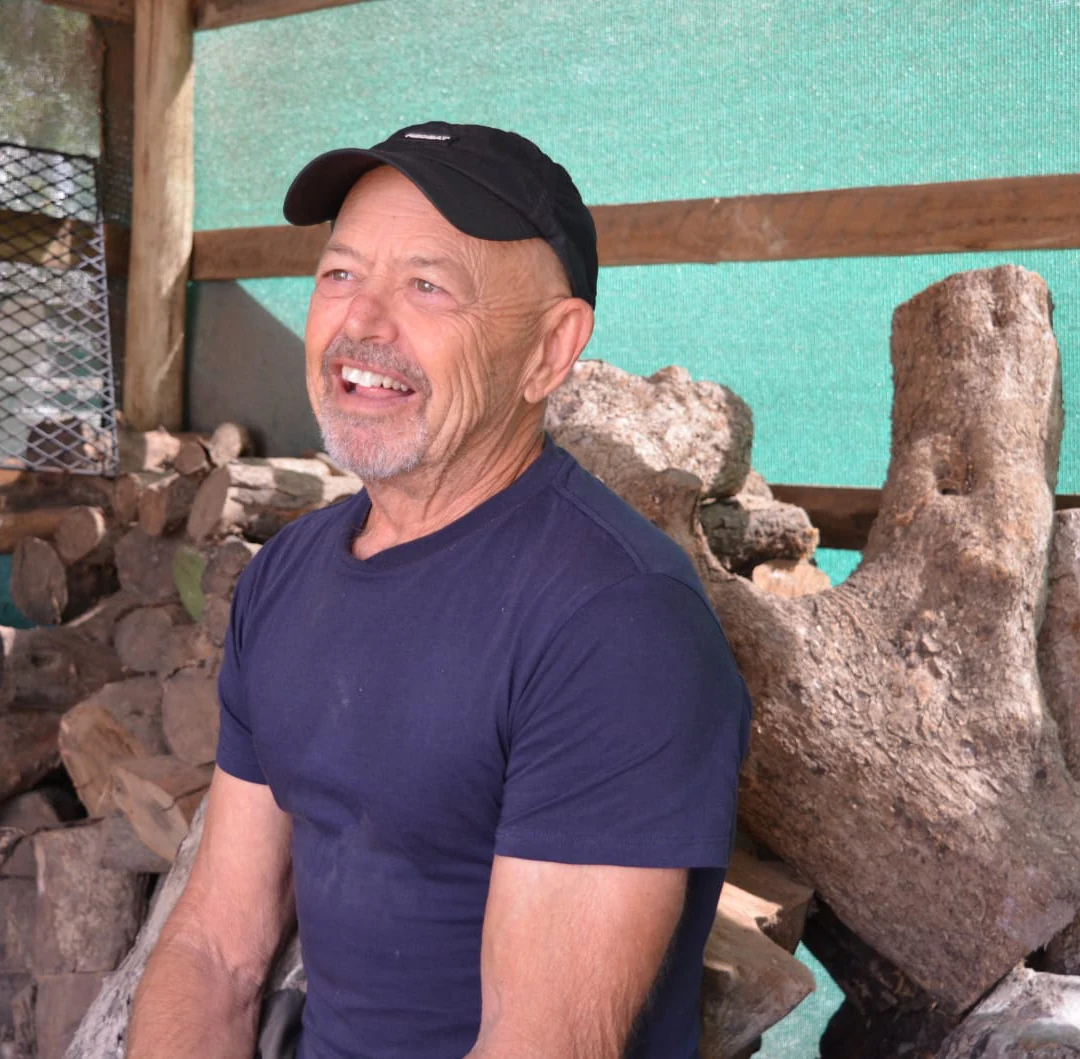 Rodney Band beside a collection of raw logs and root wood in his studio.